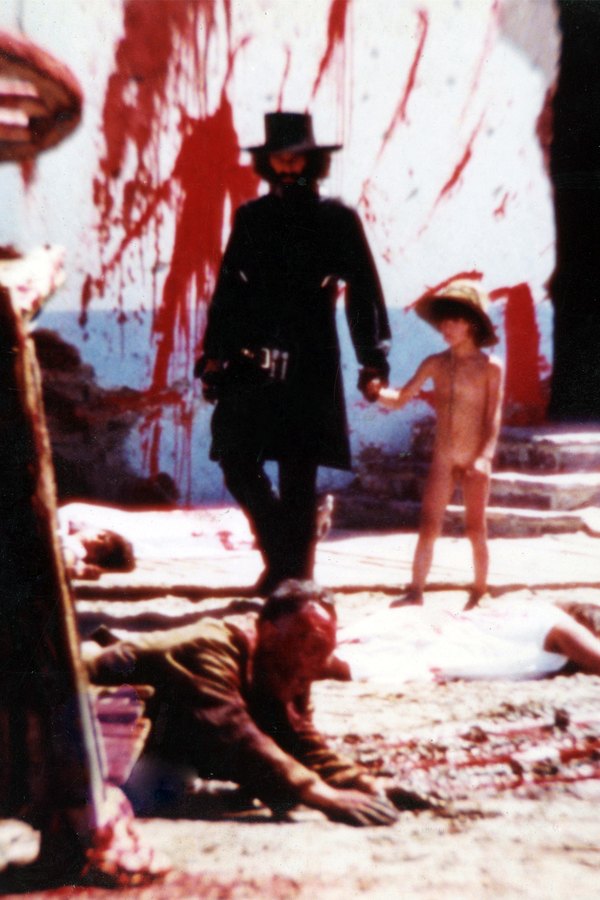 Still from El Topo: a gunfighter in black leads a child by the hand through a blood-splattered street