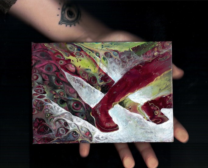 A hand holding a small poured-paint painting: a dark red boot shape stepping across white, with swirling eyes behind it